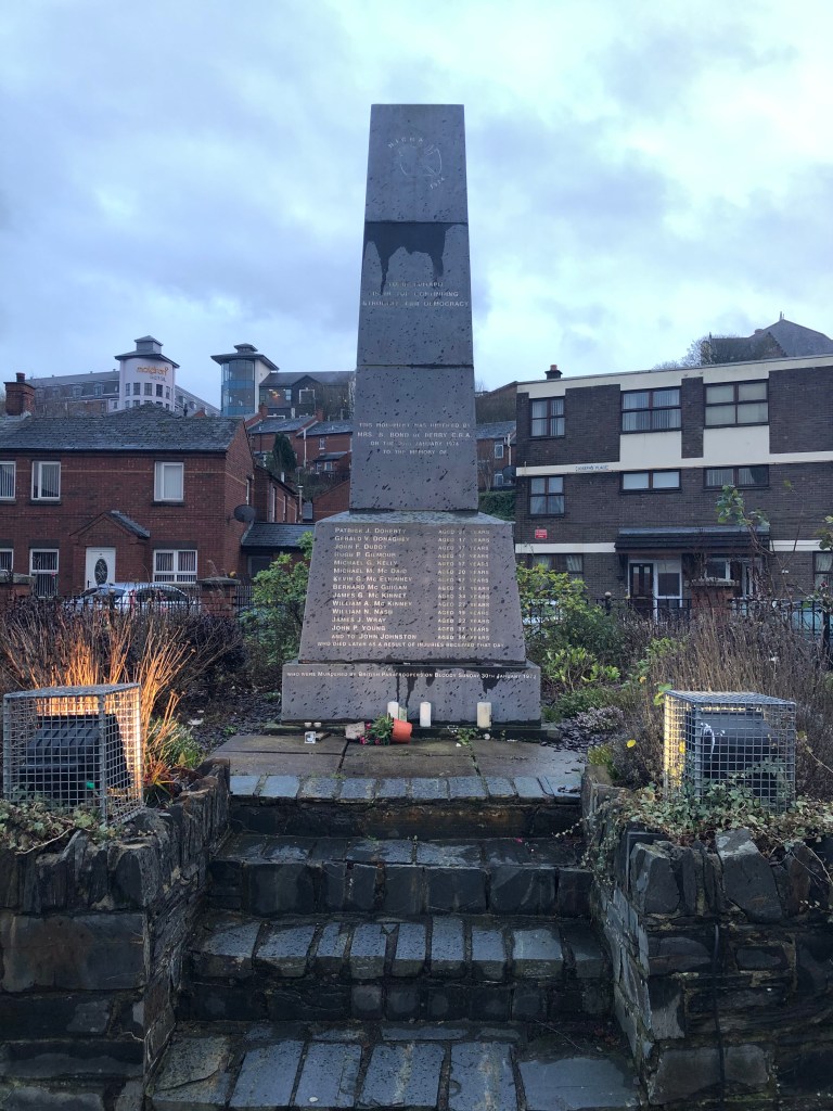 Flowers and small knick knacks sit fallen over from strong winds in front of the Bloody Sunday victim's memorial.